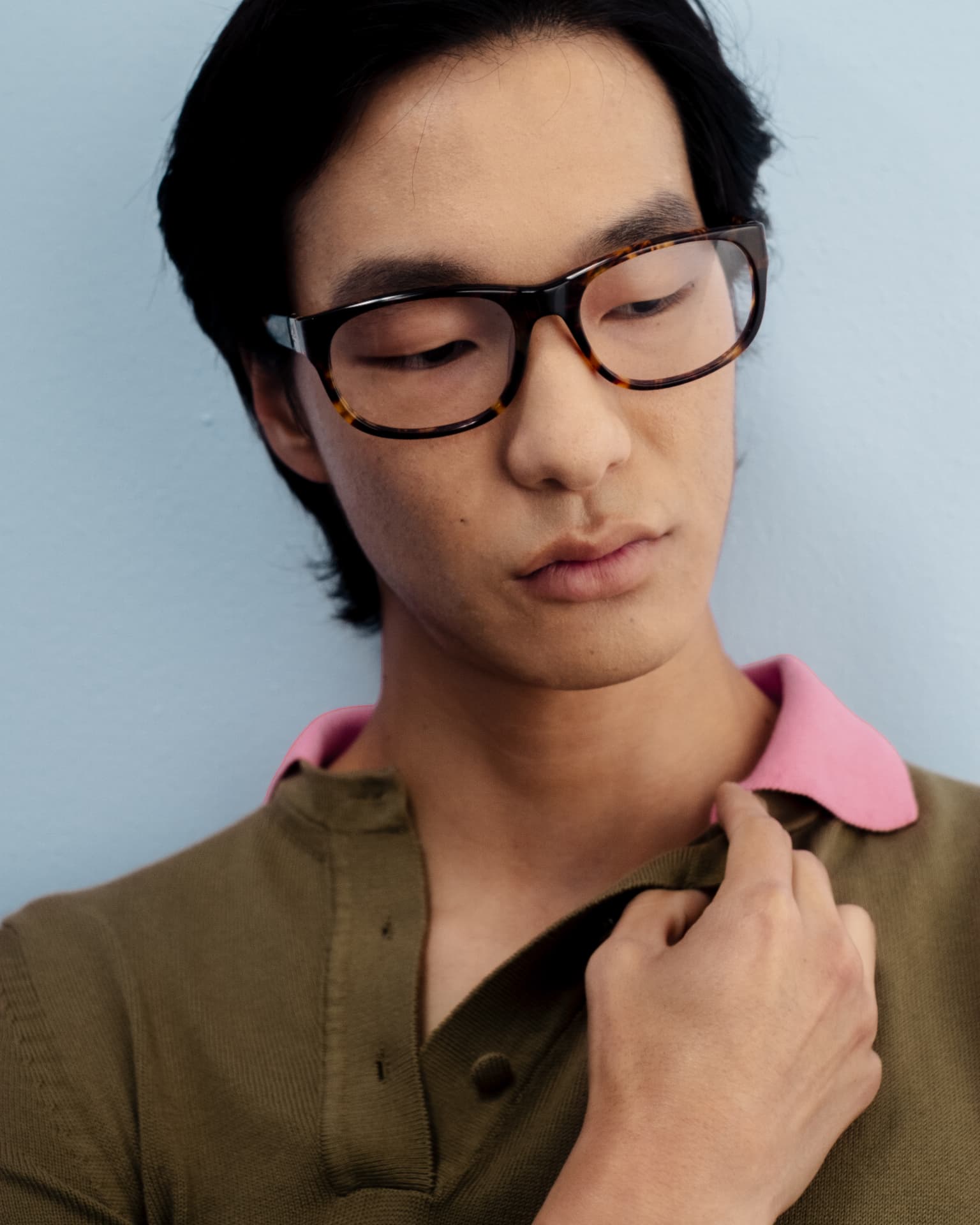 Bonnie Clyde — man in tortoise-shell glasses and an olive polo shirt, close-up portrait against light blue