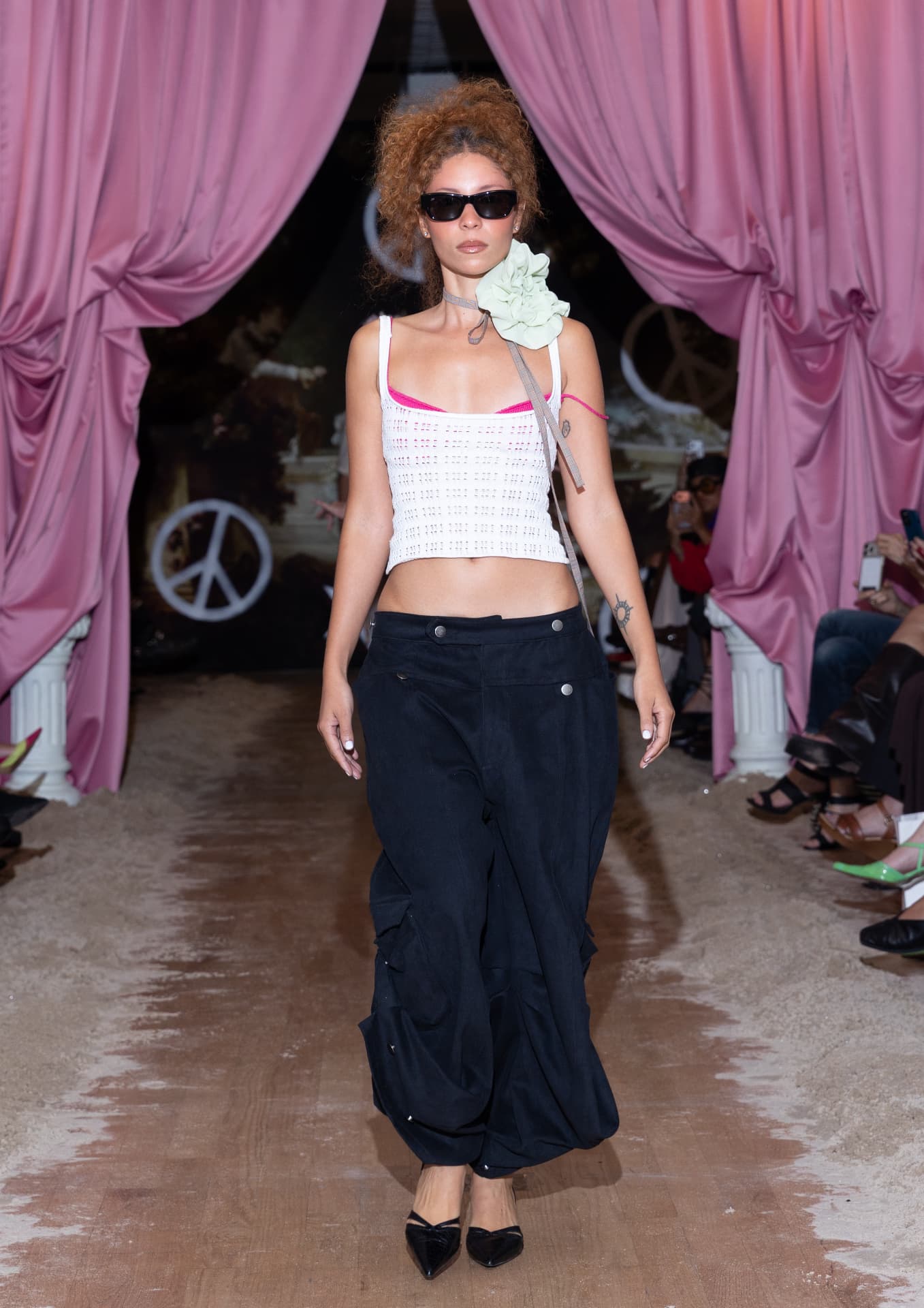 Ella Mae SS27 — white open-knit crop top with oversized black trousers and a green neck flower