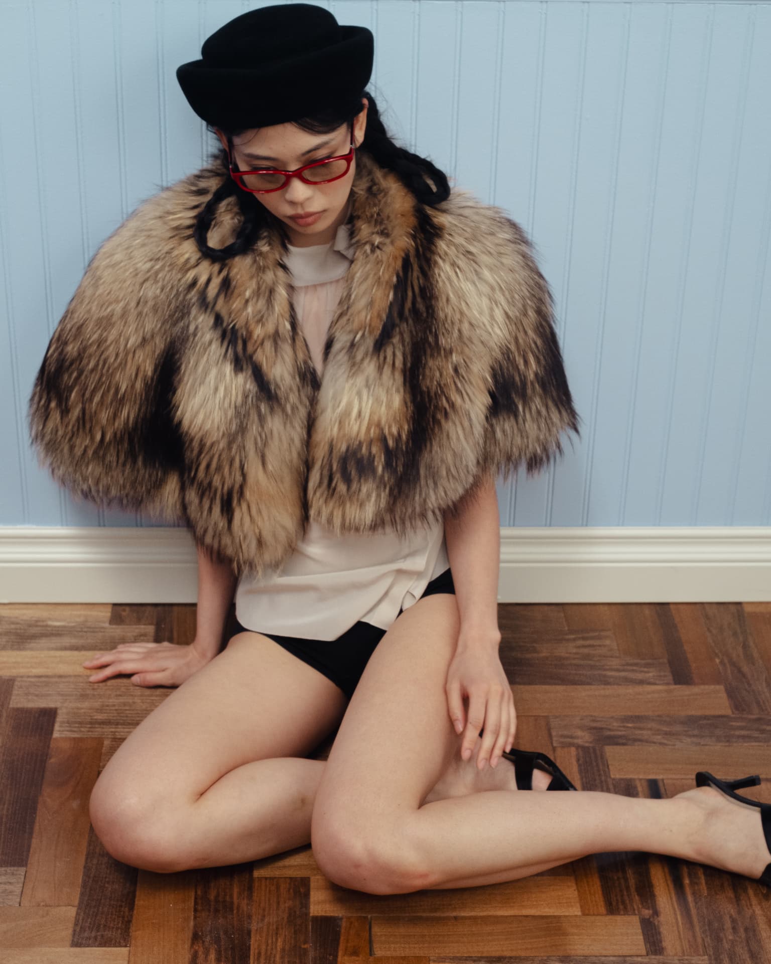 Bonnie Clyde — woman in a fur capelet and red glasses seated pensively on a parquet floor