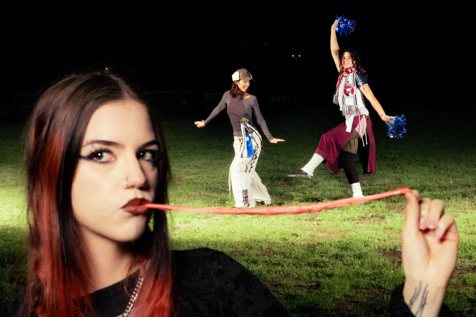 Janky Inc. Limited — a woman pulling red candy from her mouth while two friends dance behind her on a night field