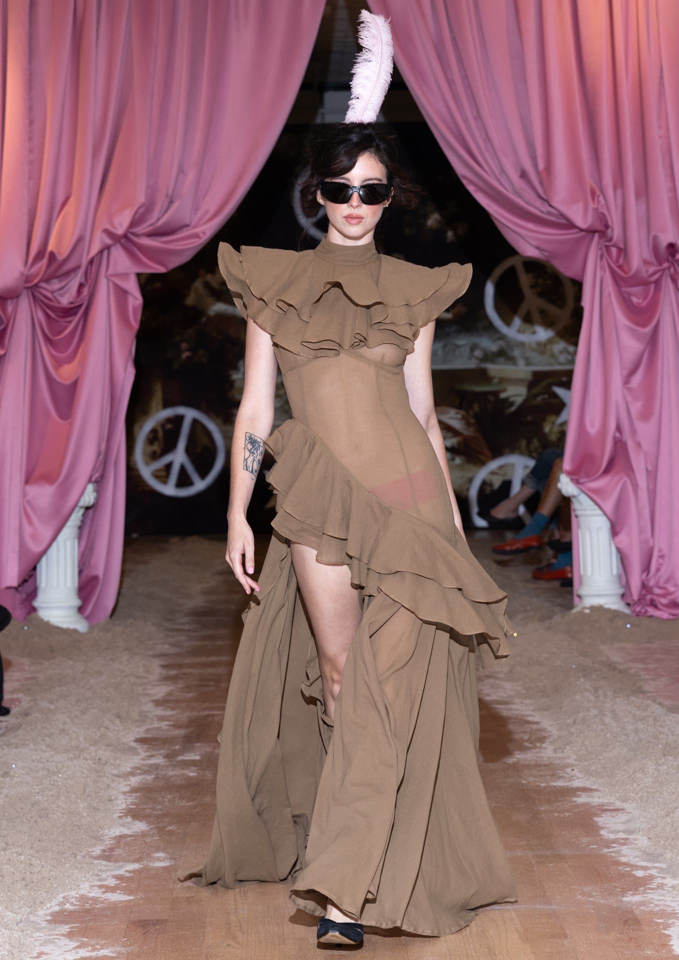 Ella Mae SS27 — sheer olive gown with cascading ruffles and a pink feather headpiece