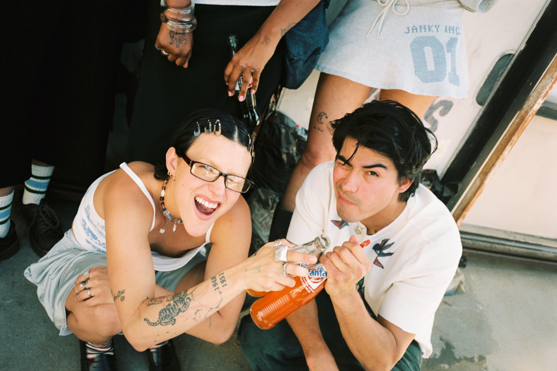 Janky Inc. SS25 — couple crouching playfully sharing an orange soda
